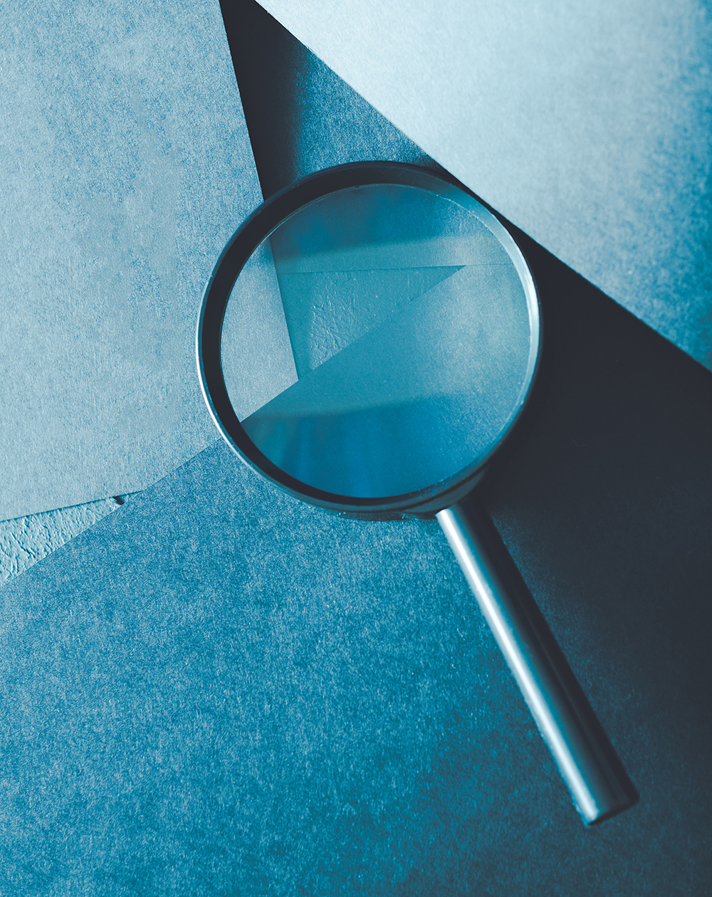 magnifying glass. science research exploration and scrutiny concept. loupe on layered blue paper background.