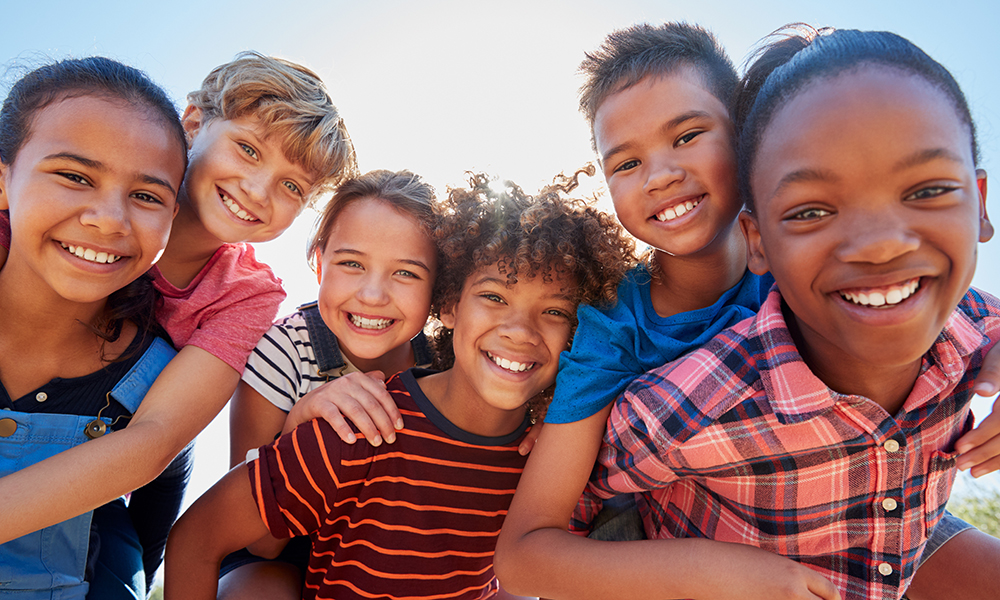 Six pre-teen friends piggybacking in a park, close up portrait